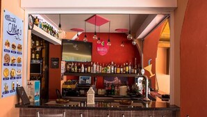 A bar area with a red wall, hanging lights, and a variety of bottles. - Nikos Studios (Zakynthos)