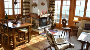 A cozy living room with a fireplace, wooden furniture, and large windows.