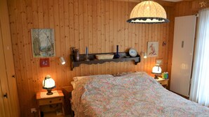 A wooden-paneled room with a bed, two bedside tables, a shelf with decorative items, and a hanging light fixture.