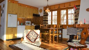 A cozy kitchen with wooden cabinets, a dining table, and chairs. There is a refrigerator, a sink, and a stove.