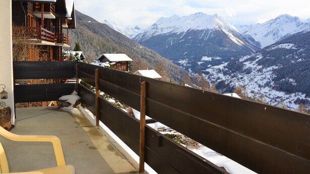 A wooden balcony with a view of snow-covered mountains.