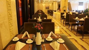 Comedor de hotel con mesas dispuestas para el servicio, un jarrón con flores y una barra de buffet al fondo.