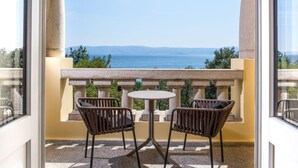 Ein Balkon mit zwei Korbstühlen und einem kleinen runden Tisch, mit Blick auf das Meer.