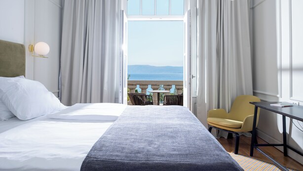 Ein Hotelzimmer mit Bett, Schreibtisch, Stuhl und Meerblick durch ein großes Fenster.