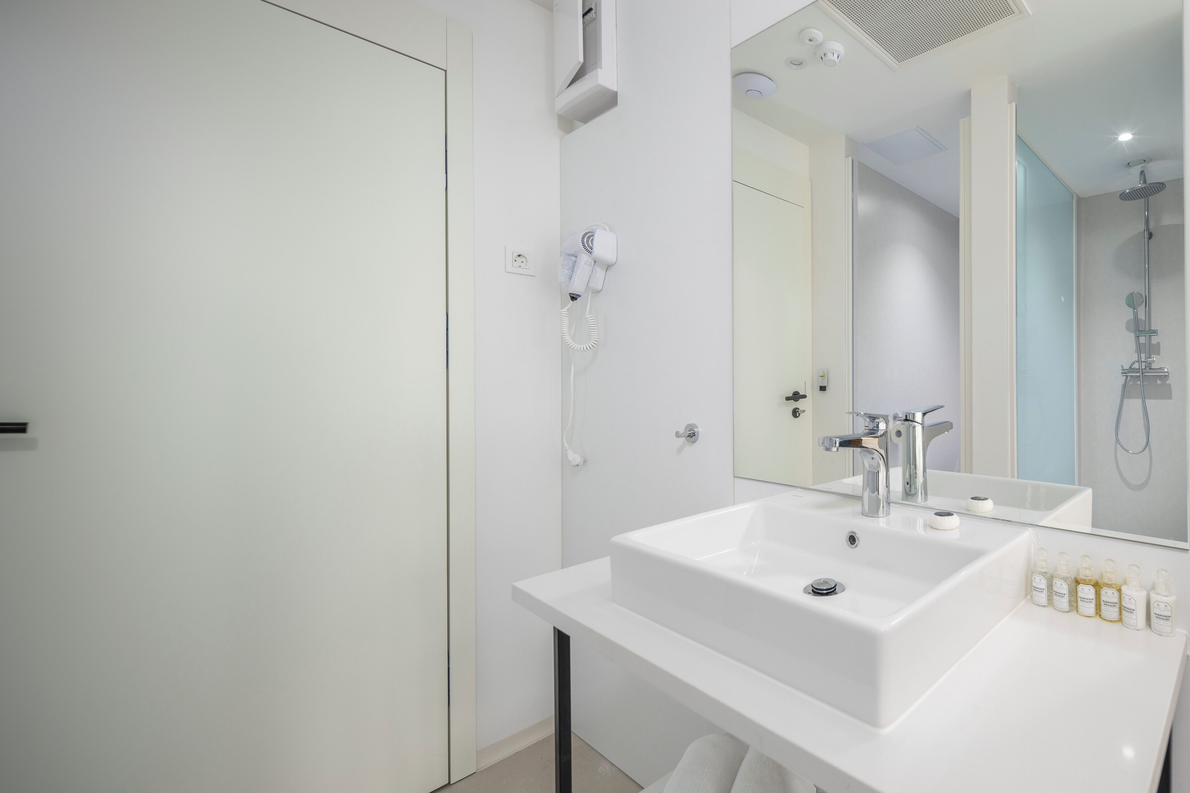 Un baño moderno con lavamanos blanco, un espejo y un cabezal de ducha manual.