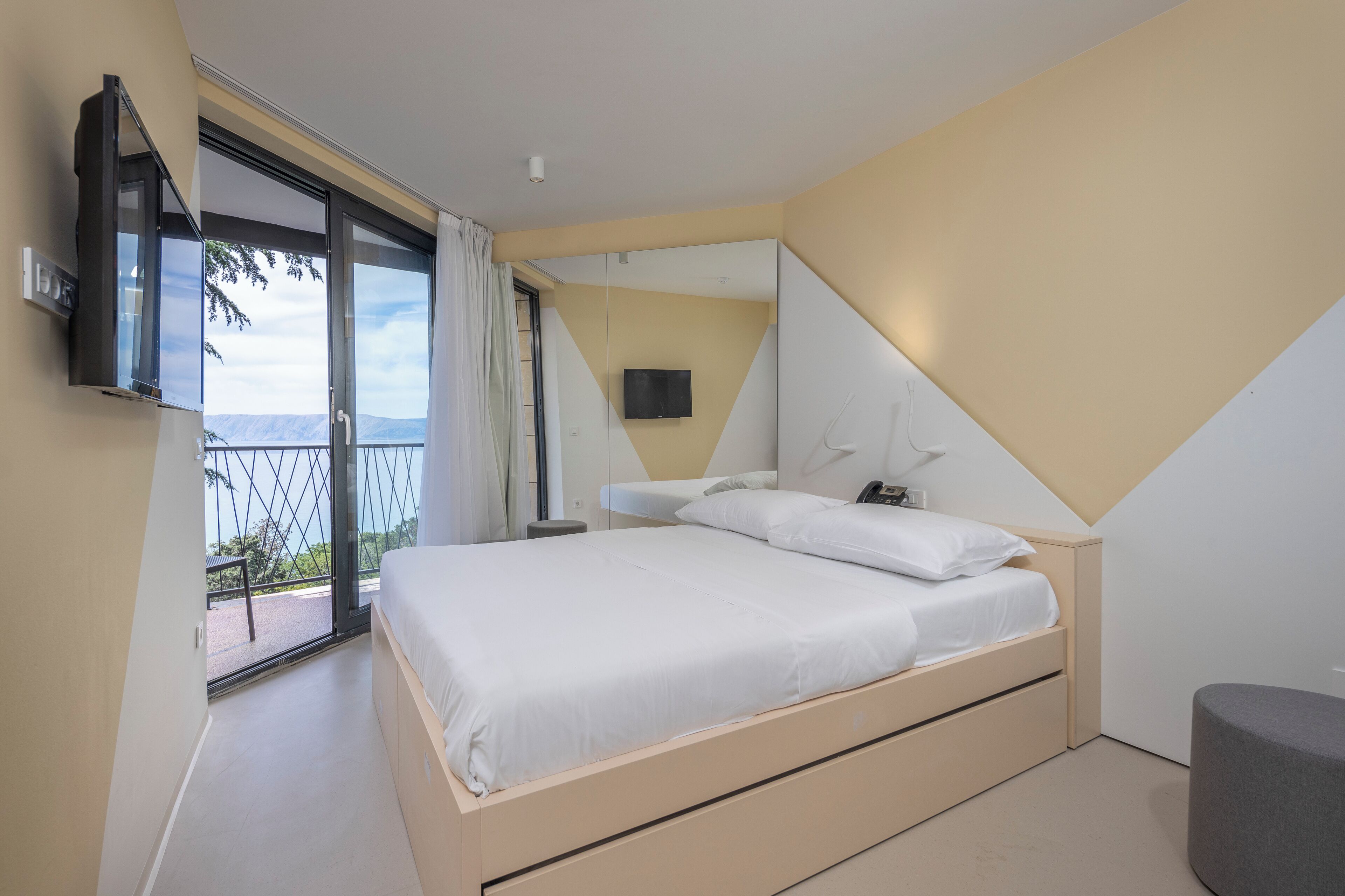 Un dormitorio moderno con cama, televisión y balcón con vistas.