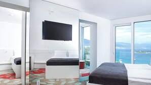 Ein modernes Hotelzimmer mit einem großen Bett, einem an der Wand befestigten Fernseher und einem Balkon mit Meerblick.