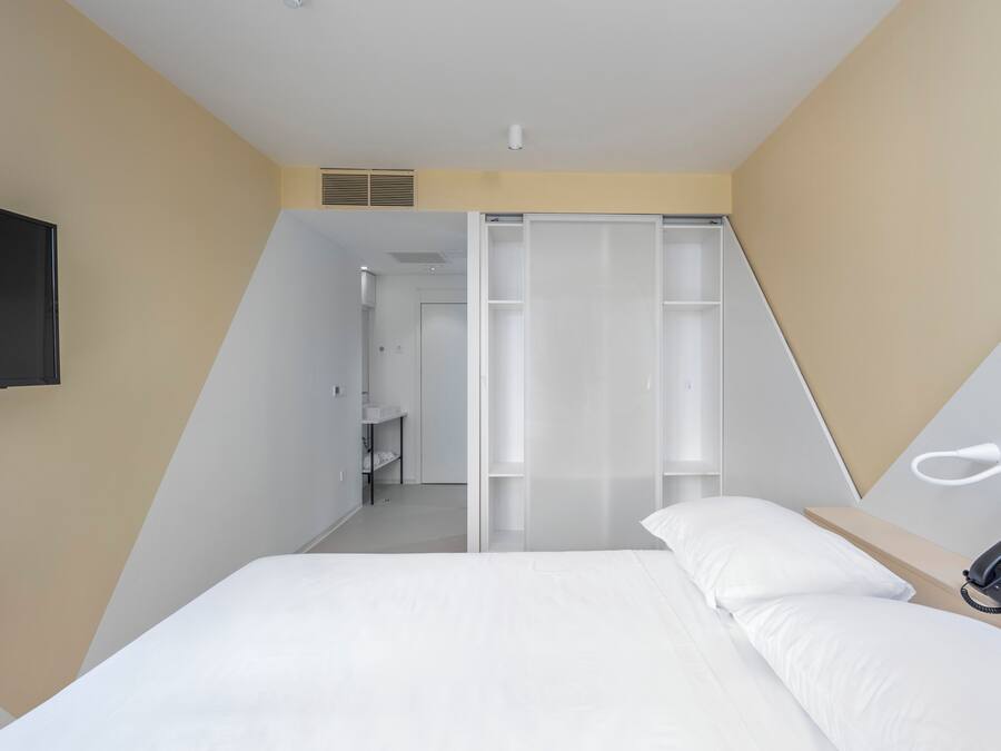 A modern hotel room with a bed, a bedside phone, and a walk-in closet with sliding doors.