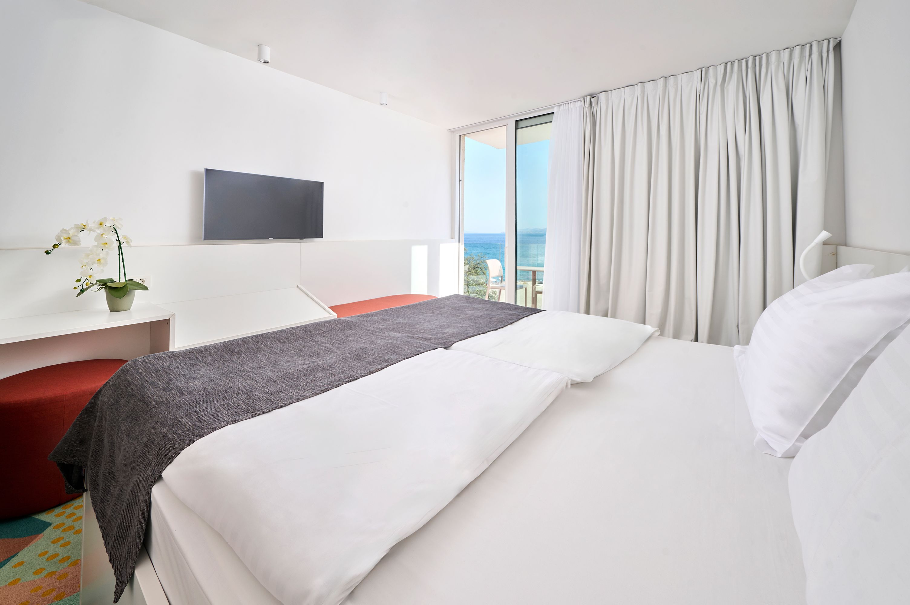 Quarto de hotel com cama, escrivaninha, cadeira, televisão e vista para o mar.