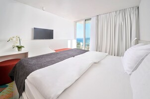 Ein Hotelzimmer mit Bett, Schreibtisch, Stuhl, Fernseher und Blick auf den Ozean.