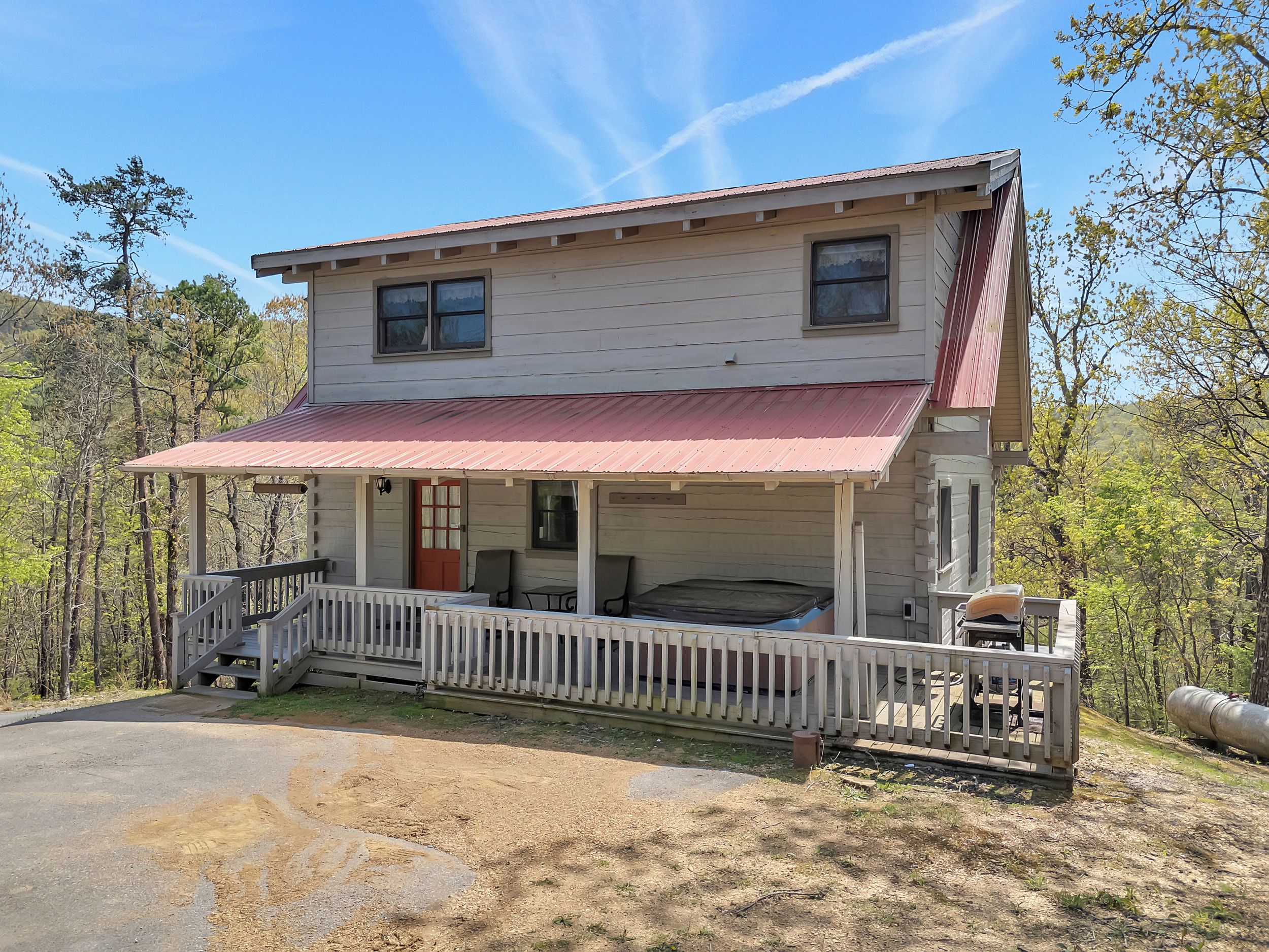 Une maison à deux étages avec un porche, un toit rouge et une vue sur la forêt environnante.