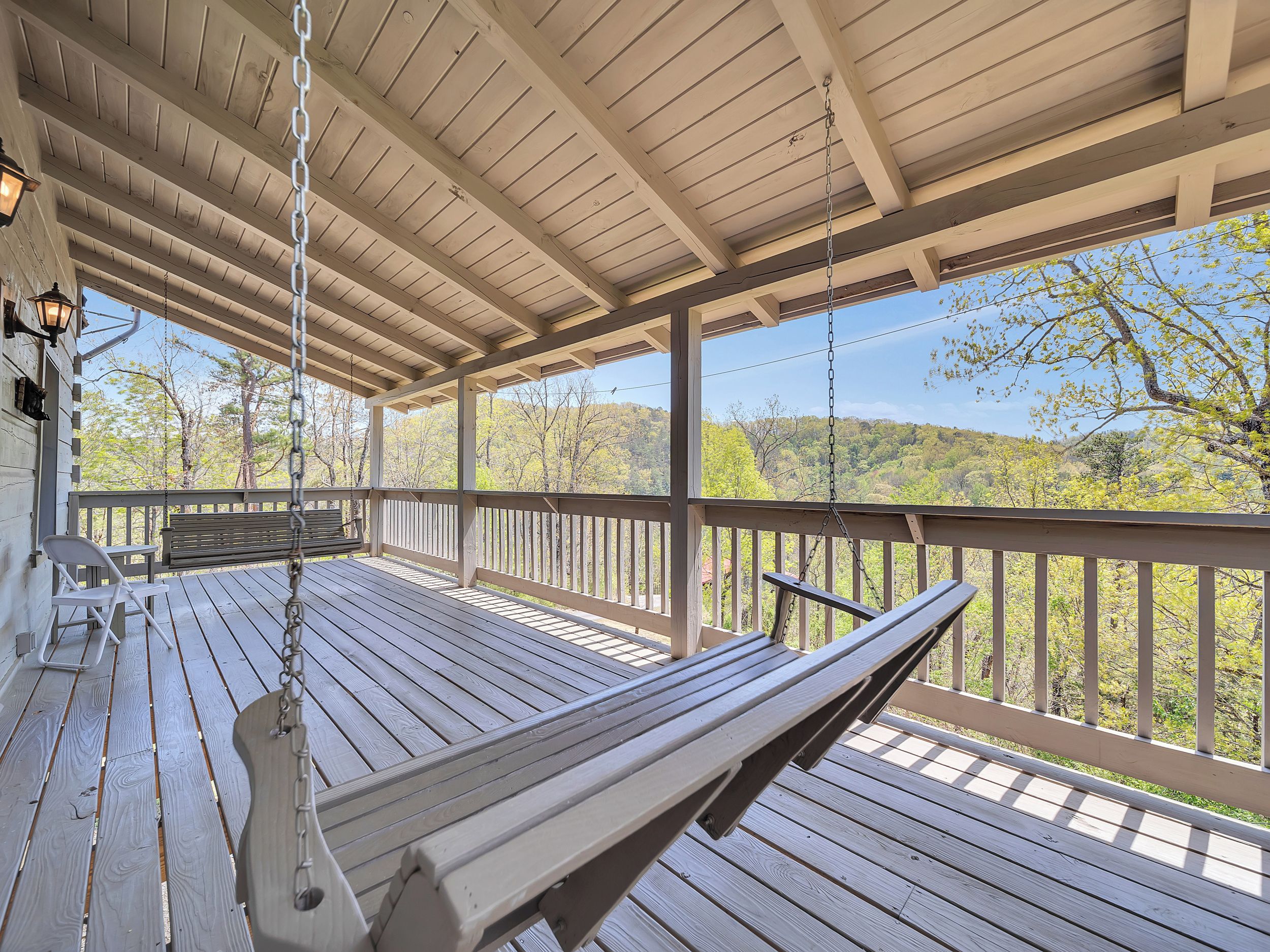 Une terrasse en bois avec une balançoire, un banc et une vue sur une colline boisée.