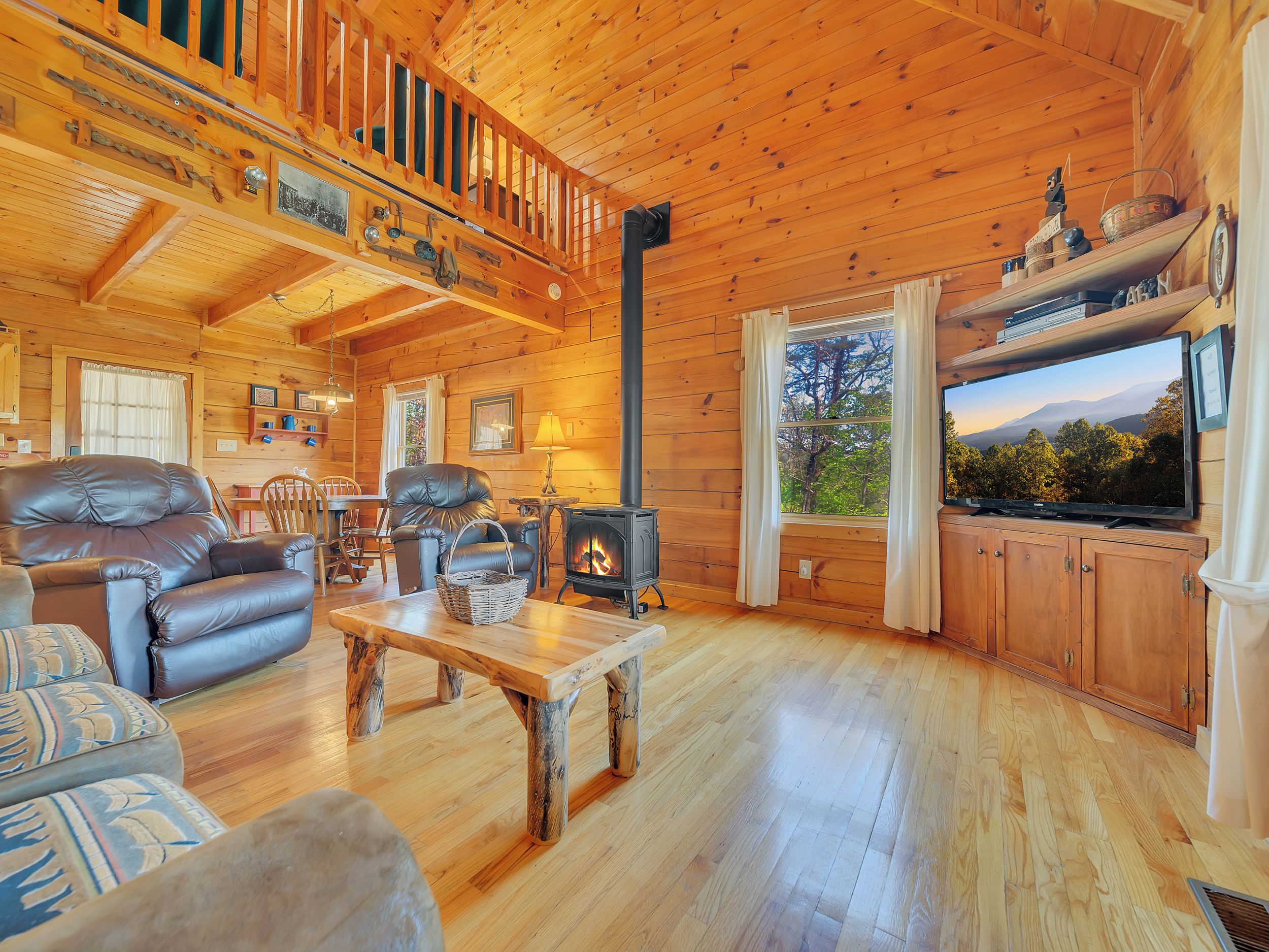 A cozy cabin interior with a fireplace, leather sofa, and a television.