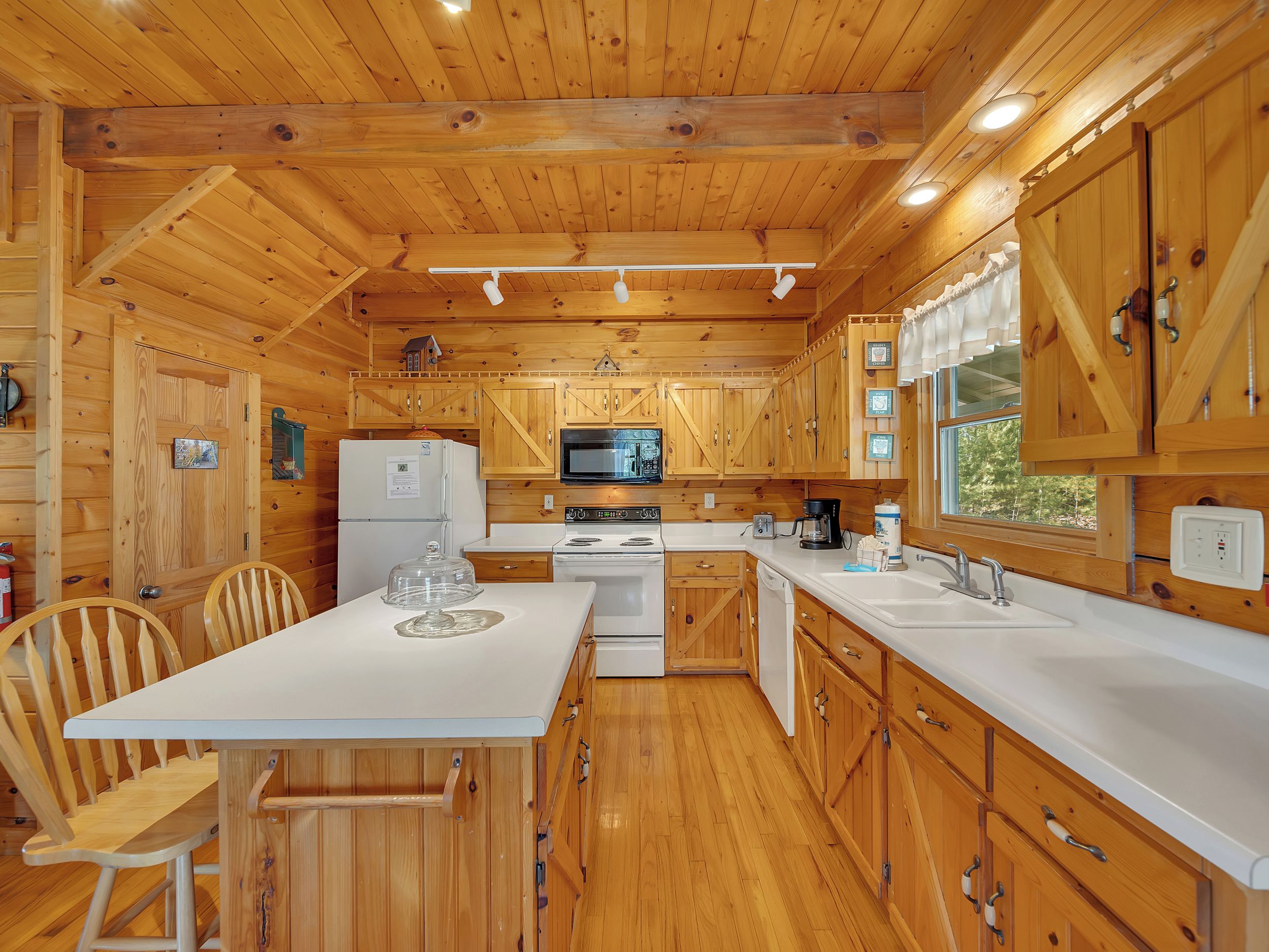 A wooden cabin interior with a kitchen area featuring a refrigerator, microwave, stove, and sink.