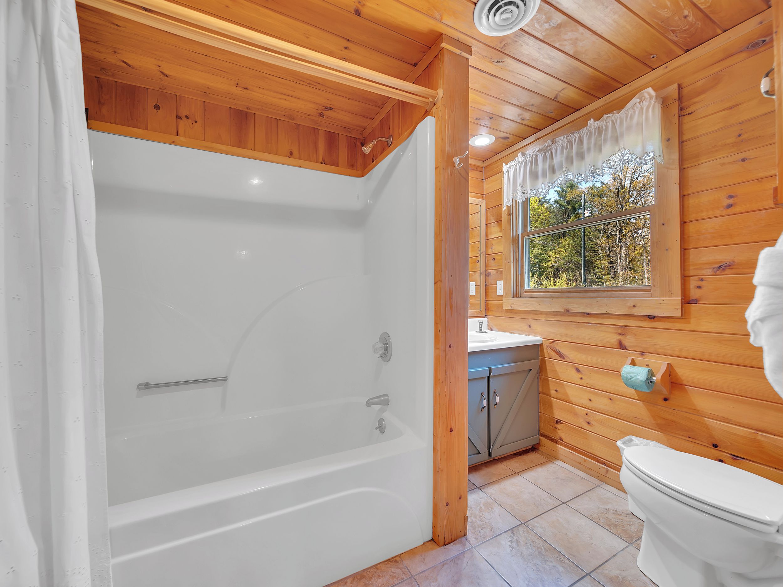 A wooden cabin bathroom with a bathtub, toilet, sink, and window.