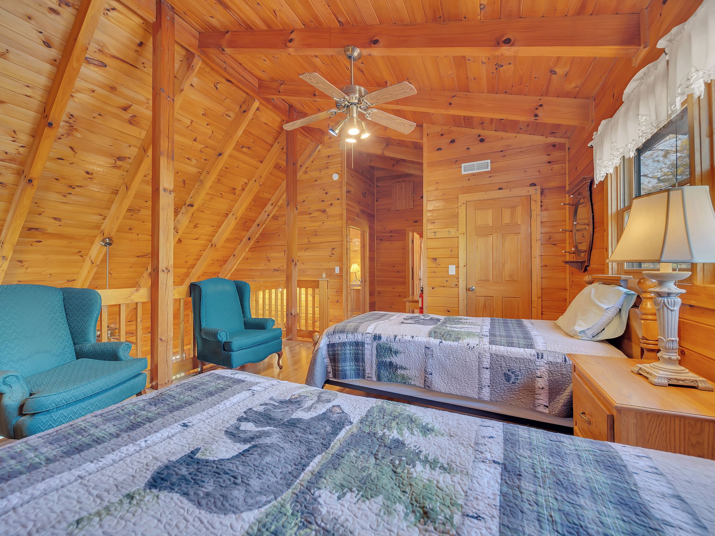 Une chambre confortable de style cabane, avec deux lits, un ventilateur de plafond et des murs en bois.