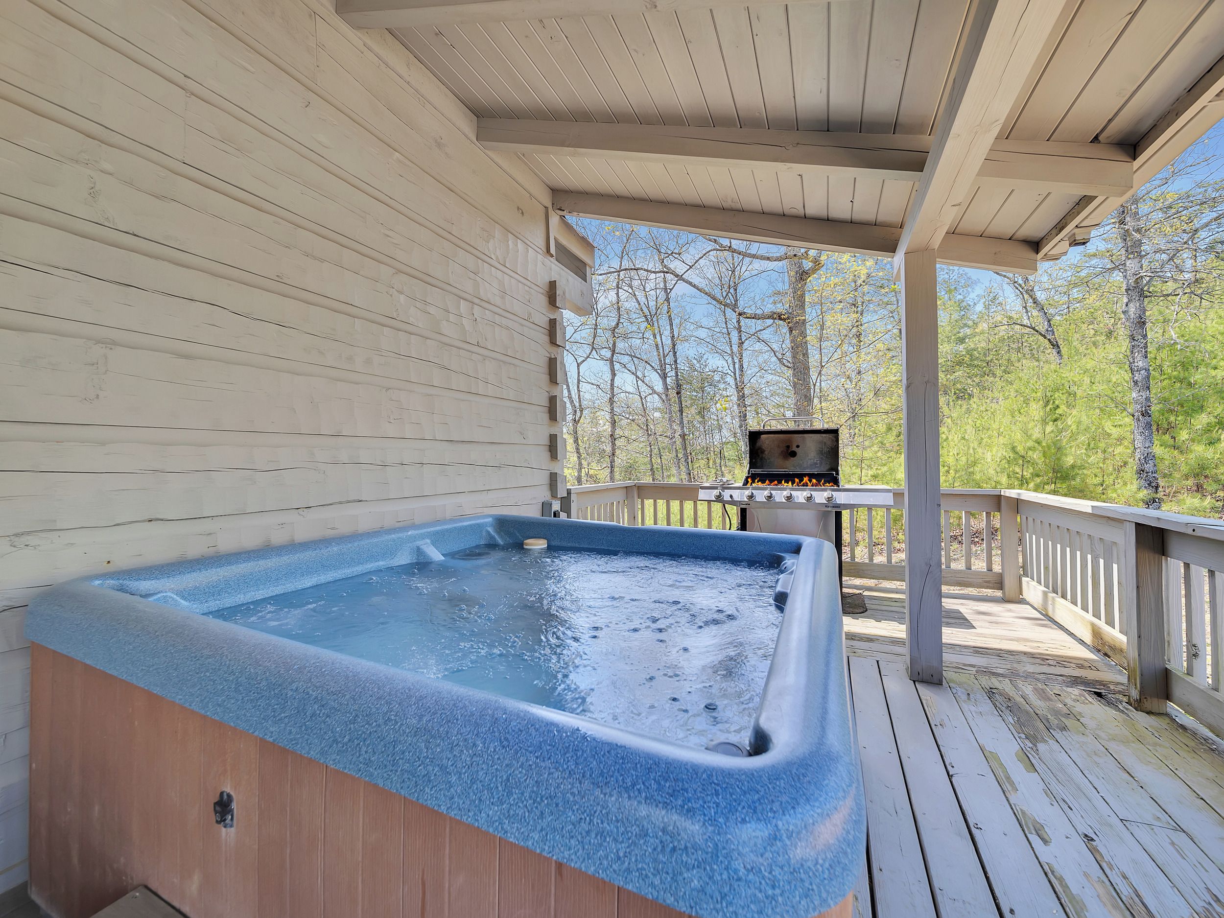 Un bain à remous sur une terrasse en bois, avec un barbecue en arrière-plan.