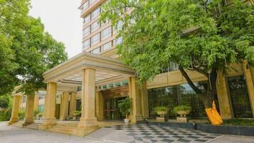 A hotel entrance with a covered patio, a checkered pavement, and lush greenery.