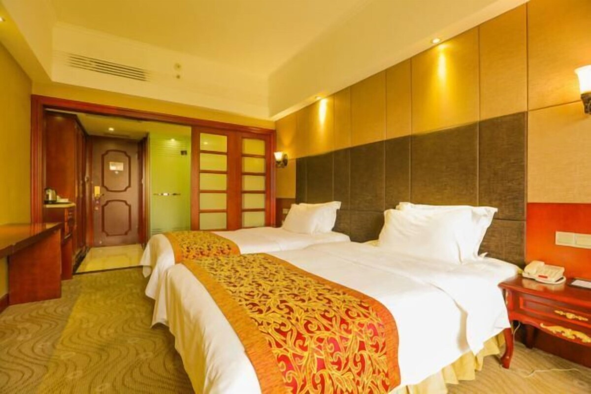 Une chambre d’hôtel avec deux lits, un bureau en bois, un téléphone et une porte donnant sur une autre pièce.