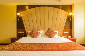 Une chambre d’hôtel avec un grand lit, deux tables de chevet, une tête de lit ornée d’un motif en forme de ventilateur et des lampes fixées au mur.