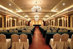 Une salle de conférence avec des rangées de tables et de chaises, un lustre et des appliques murales.