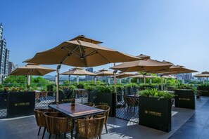 Espace extérieur aménagé avec des parasols, des tables et des chaises, entouré de verdure et offrant une vue sur le paysage urbain.