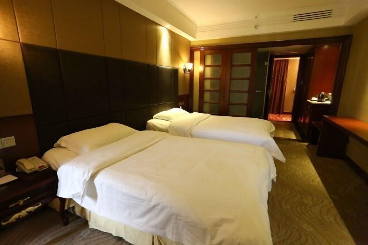 Une chambre d’hôtel avec deux lits, un bureau avec un téléphone et une armoire en bois.