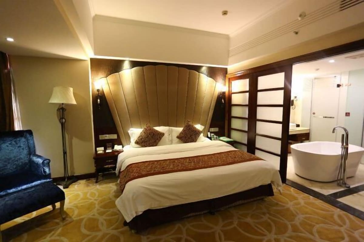 Une chambre d’hôtel avec un grand lit, un coin salon, une salle de bain avec baignoire et un grand miroir.