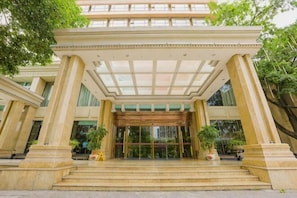 Una entrada imponente con puerta de cristal, columnas y un corredor cubierto.