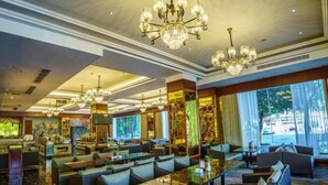 Un amplio vestíbulo de hotel con varias zonas de estar, grandes candelabros y ventanales que ofrecen vistas al exterior.