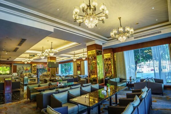 Un amplio vestíbulo de hotel con varias zonas de estar, grandes candelabros y ventanales que ofrecen vistas al exterior.