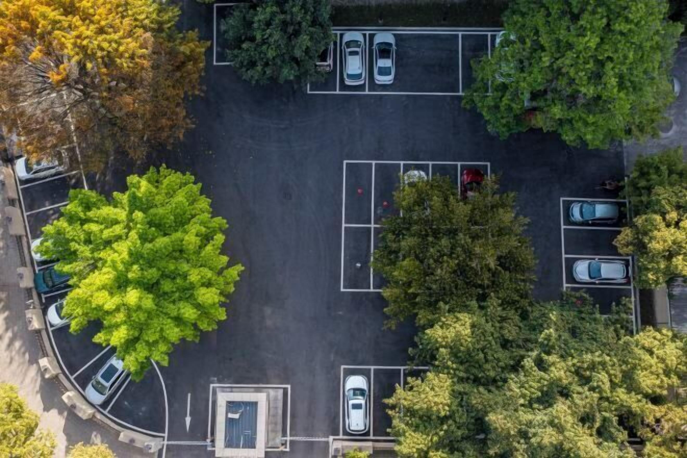 An aerial view of a parking lot with multiple parking spaces and trees surrounding it.
