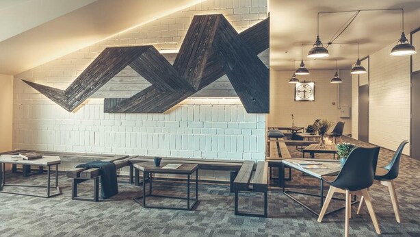 A modern office space with a high ceiling, exposed brick walls, and a large wooden geometric wall feature. There are multiple tables and chairs arranged for meetings. - Railway Apartments (Vilnius)