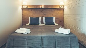 A hotel room with a wooden headboard, two bedside lamps, a bed with a grey checkered bedspread, and two folded towels on the bed. - Railway Apartments (Vilnius)