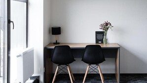A modern office space with a desk, two black chairs, a lamp, and a vase with flowers. - Railway Apartments (Vilnius)