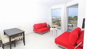 A modern living room with a dining table, two red sofas, and a small side table. - Meandros Hotel Apts (Protaras)