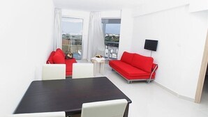 A modern room with a dining table, two red sofas, a TV, and a balcony with a view. - Meandros Hotel Apts (Protaras)