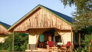 A rustic wooden cabin with a covered porch, two chairs, and a table. - Africa Safari Serengeti Ikoma (Serengeti)