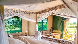 A tented room with a bed, a table with chairs, and a view of greenery outside. - Africa Safari Serengeti Ikoma (Serengeti)
