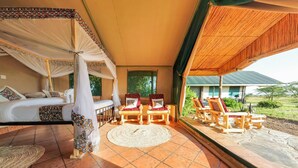 A tented room with a bed, a sitting area with chairs, and a view of the outdoors. - Africa Safari Serengeti Ikoma (Serengeti)