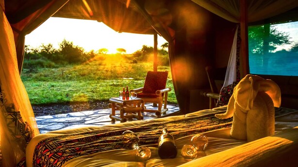 A cozy room with a bed, a chair, a small table with bottles, and a blanket. - Africa Safari Serengeti Ikoma (Serengeti)