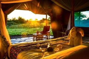 A cozy room with a bed, a chair, a small table with bottles, and a blanket. - Africa Safari Serengeti Ikoma (Serengeti)