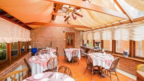 Un restaurant aux murs de briques, aux poutres apparentes et aux tables recouvertes de nappes blanches, avec des chaises assorties.