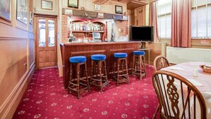 Un espace bar avec des tabourets en bois, un comptoir avec un téléviseur et des tableaux encadrés au mur.