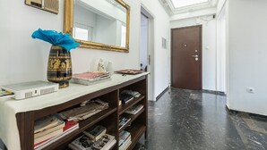 A hallway with a white wall, a large mirror, a wooden console table with books and a vase, and a door at the end. - Acropolis View dream apartment (Athina)