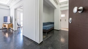 A hotel room with a dark marble floor, a blue sofa, a wooden desk with a television, and a door with a silver handle. - Acropolis View dream apartment (Athina)