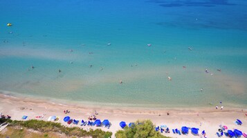 Una playa con agua cristalina, gente nadando y sombrillas en la arena.