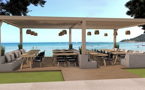 An outdoor seating area with tables and chairs, overlooking a beach with boats and people. - Alykanas Village Resort (Zakynthos)