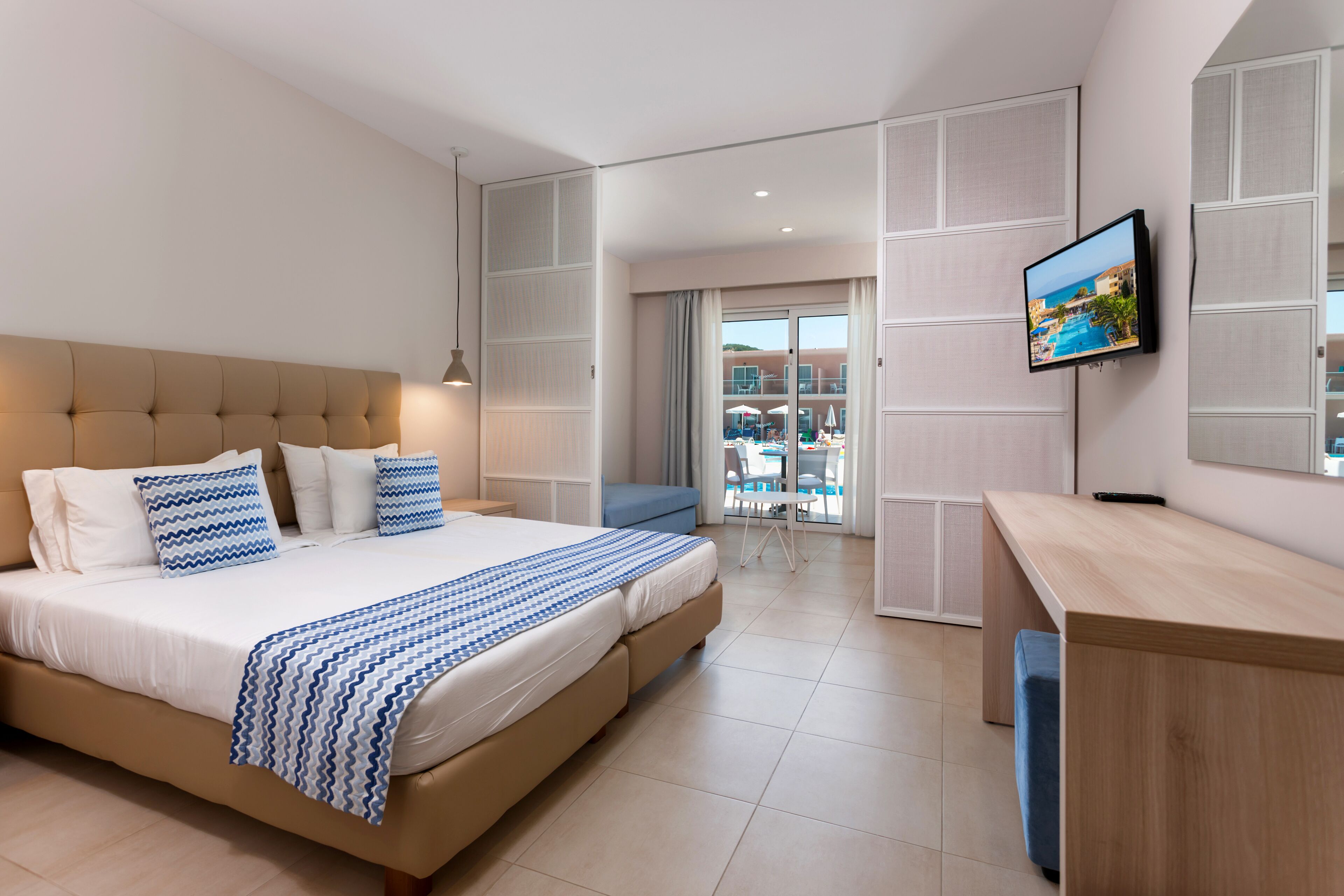 A modern hotel room with a large bed, a desk, and a TV on the wall.