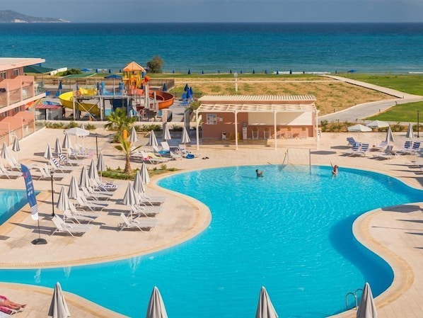 A pool area with lounge chairs and umbrellas, a water slide, and a view of the sea.